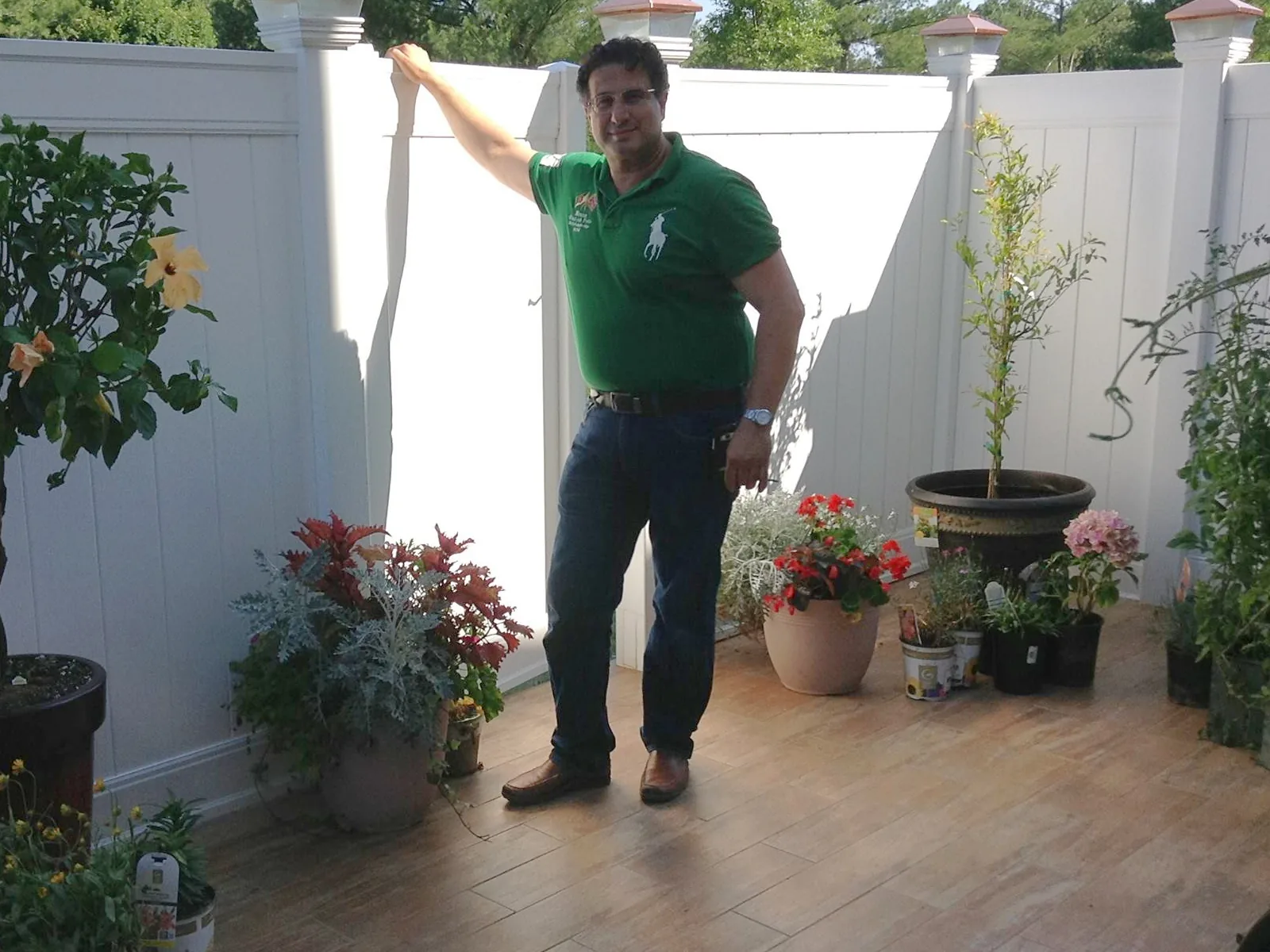 Jonathan Abecassis standing on a tiled patio beside a white privacy fence, surrounded by potted plants
